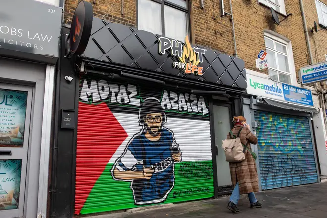Artwork featuring an image of Palestinian journalist Motaz Azaiza on a Palestinian flag painted on a shop blind in Tower Hamlets.