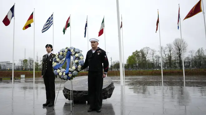 Two military personnel stand underneath the flags of Nato alliance members during a wreath-laying ceremony at Nato headquarters in Brussels