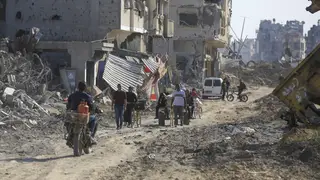 Palestinians walk through the destruction left by the Israeli air and ground offensive after they withdrew from Khan Younis, southern Gaza Strip