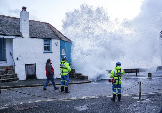 Coastguard personnel look on as waves crash over the harbour wall onto the street on in St Ives, Cornwall