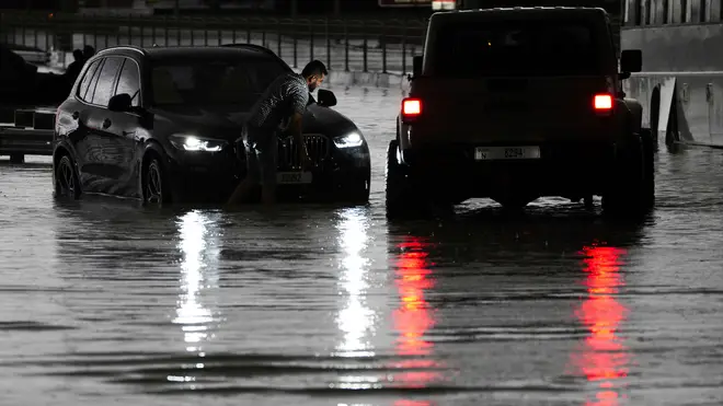A man tries to work on his stalled SUV in standing water in Dubai