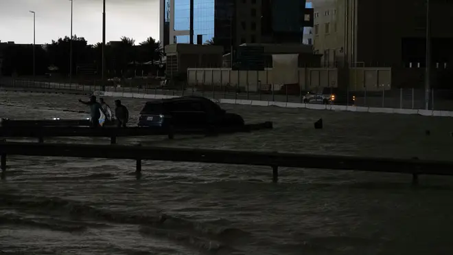 Men gesture as they try to tow a vehicle out of standing water in Dubai