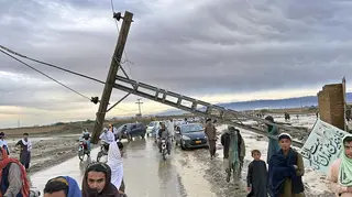 People pass by a damaged electric pole caused by flooding due to heavy rains in Pakistan