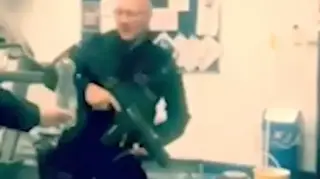 The officer can be seen clutching his G36 assault rifle as he kicks the bottle top off.