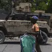A man carries dry cleaning past an armoured police vehicle in Port-au-Prince, Haiti