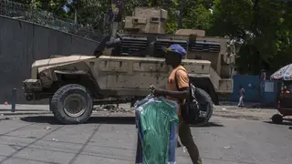 A man carries dry cleaning past an armoured police vehicle in Port-au-Prince, Haiti