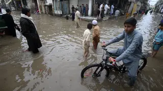 Youngsters wade through a flooded street caused by heavy rain in Peshawar, Pakistan