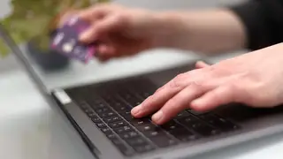 A woman using a laptop and holding a debit card