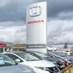 Cars for sale outside a Honda dealership with large Honda logo on signage.