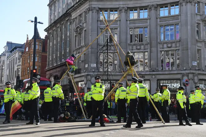 Police attempt to remove a protester that is sat on top of a bamboo structure built to block the road at Oxford Circus