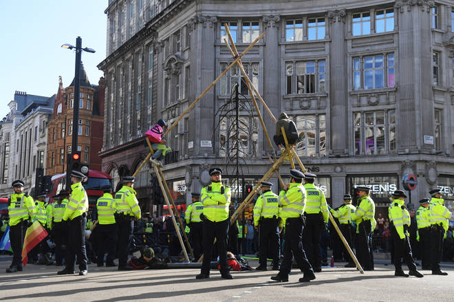 Police attempt to remove a protester that is sat on top of a bamboo structure built to block the road at Oxford Circus