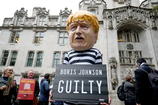A man wearing a giant Boris Johnson mask and prison clothing