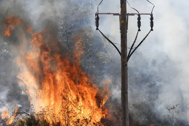 Flames erupt in the tall brush surrounding an electrical pole on a hillside in California