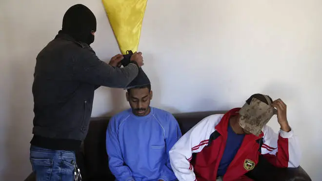 A Kurdish security officer takes off face masks from Alexanda Amon Kotey, left, and El Shafee Elsheikh
