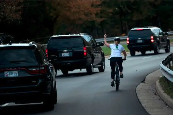 Juli Briskman gestures with her middle finger as a motorcade with US President Donald Trump departs Trump National Golf Course