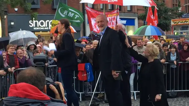 Jeremy Corbyn laughs as he stays dry under an umbrella