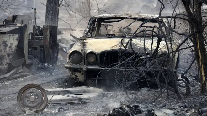 The burnt out shell of a Jaguar vehicle sits in the ruins of a smouldering house in New South Wales