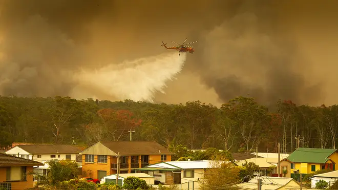 A helicopter drops water on fires in an attempt to save houses