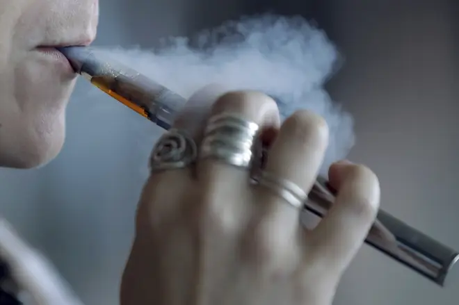 A woman using a vaping device exhales a puff of smoke