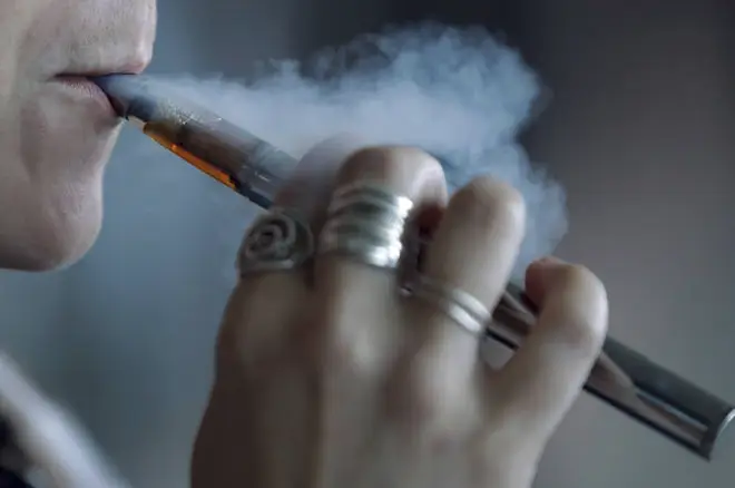 A woman using a vaping device exhales a puff of smoke.