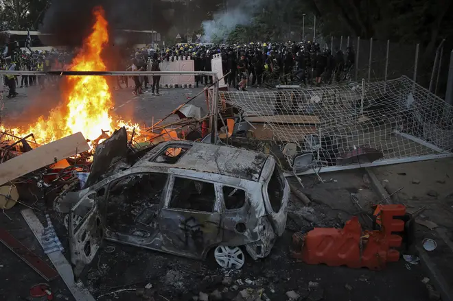 Students stand near a fire and a charred vehicle during a face-off with riot police