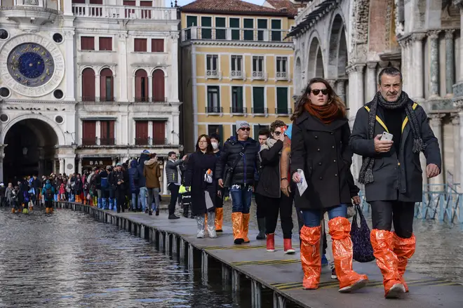 People in wellies walk on a footbridge across the flooded St. Mark's Square