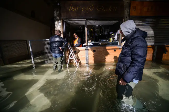 A man walks past a cafe across a flooded arcade by St. Mark's Square