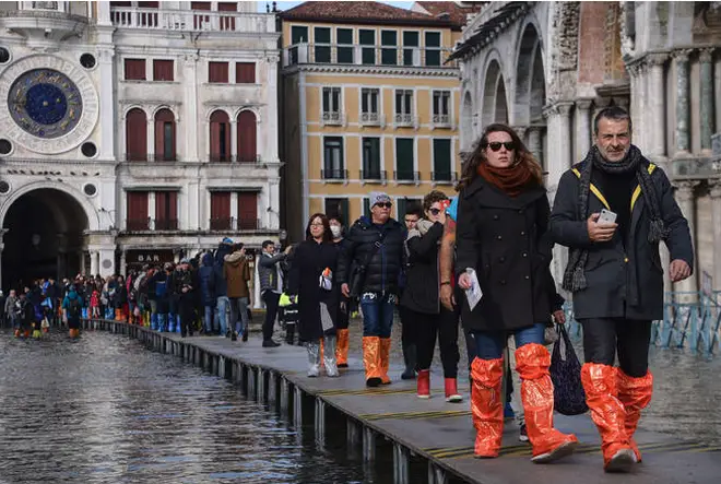 People in wellies walk on a footbridge across the flooded St. Mark's Square.