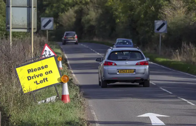 A vehicle with diplomatic plates passes a Please Drive on Left sign and road marking that have been placed on the B4031 outside RAF Croughton, in Northamptonshire, where Harry Dunn died